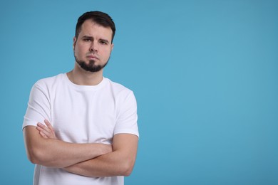 Photo of Portrait of sad man with crossed arms on light blue background, space for text