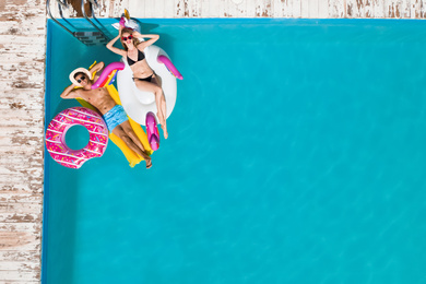 Happy couple with inflatable rings and mattress in swimming pool, top view. Summer vacation