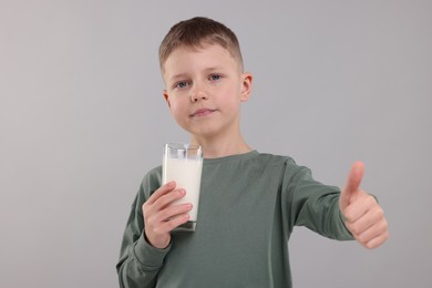 Photo of Cute boy with glass of fresh milk showing thumb up on light grey background