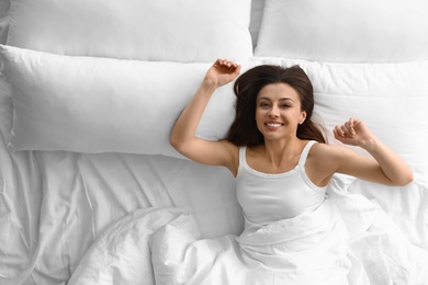 Portrait of beautiful young woman awakening in large bed, above view