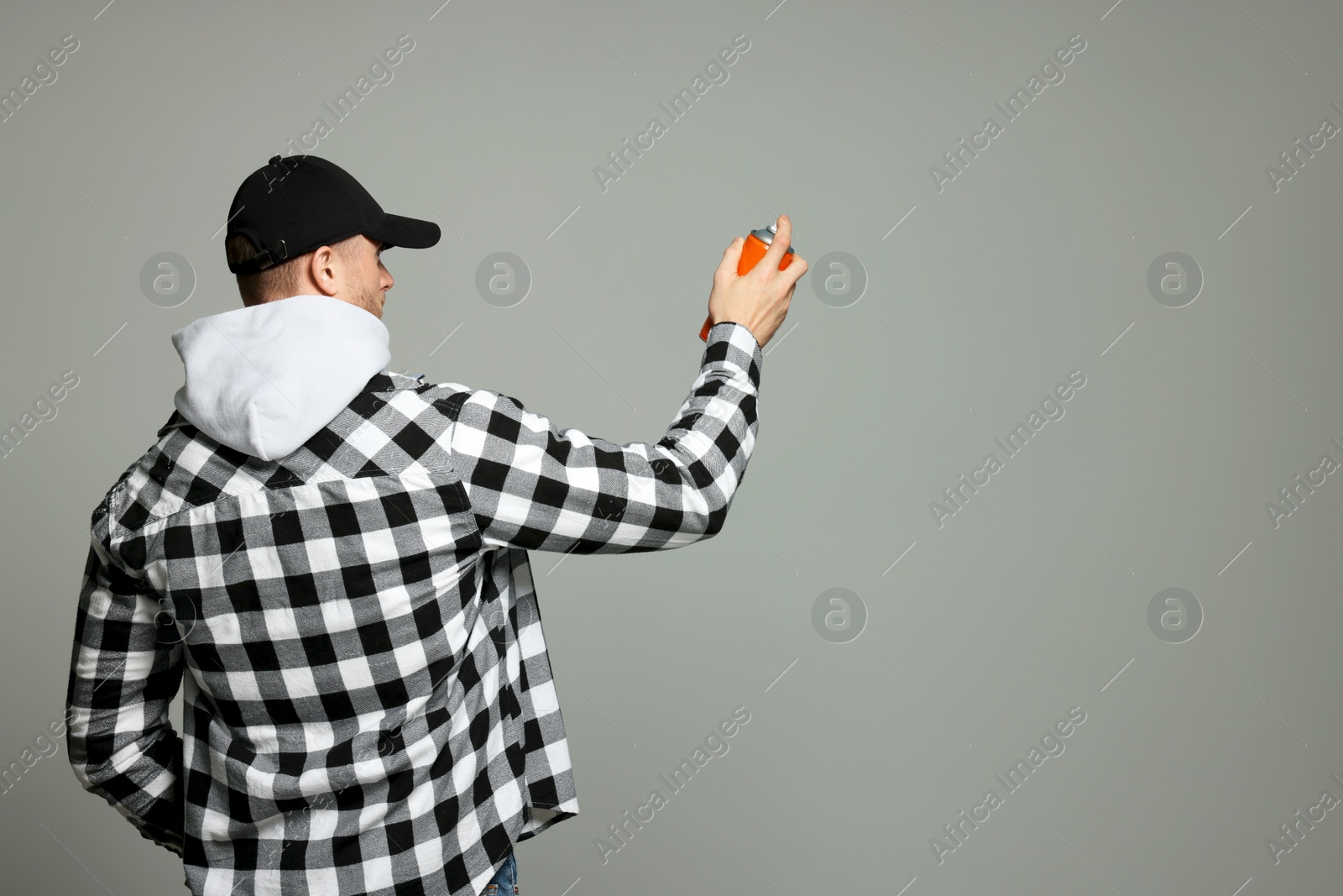 Photo of Man holding orange can of spray paint on grey background, back view. Space for text