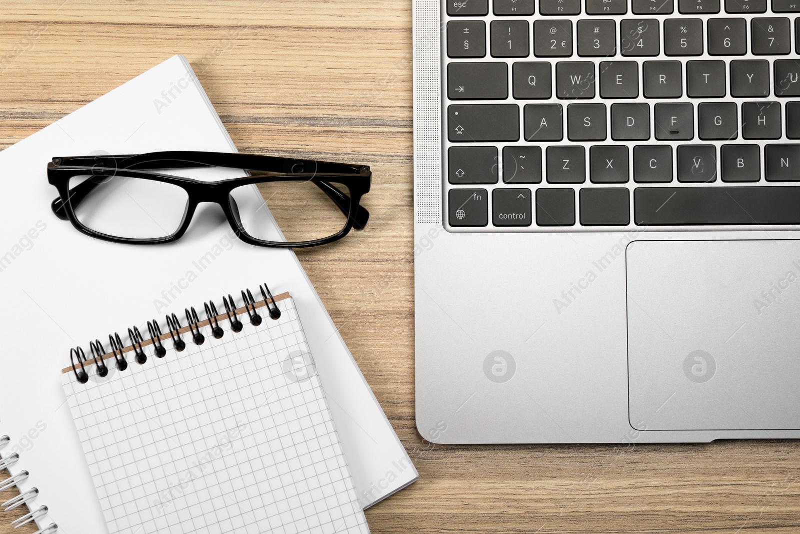 Photo of Modern laptop, notebooks and glasses on wooden table, flat lay