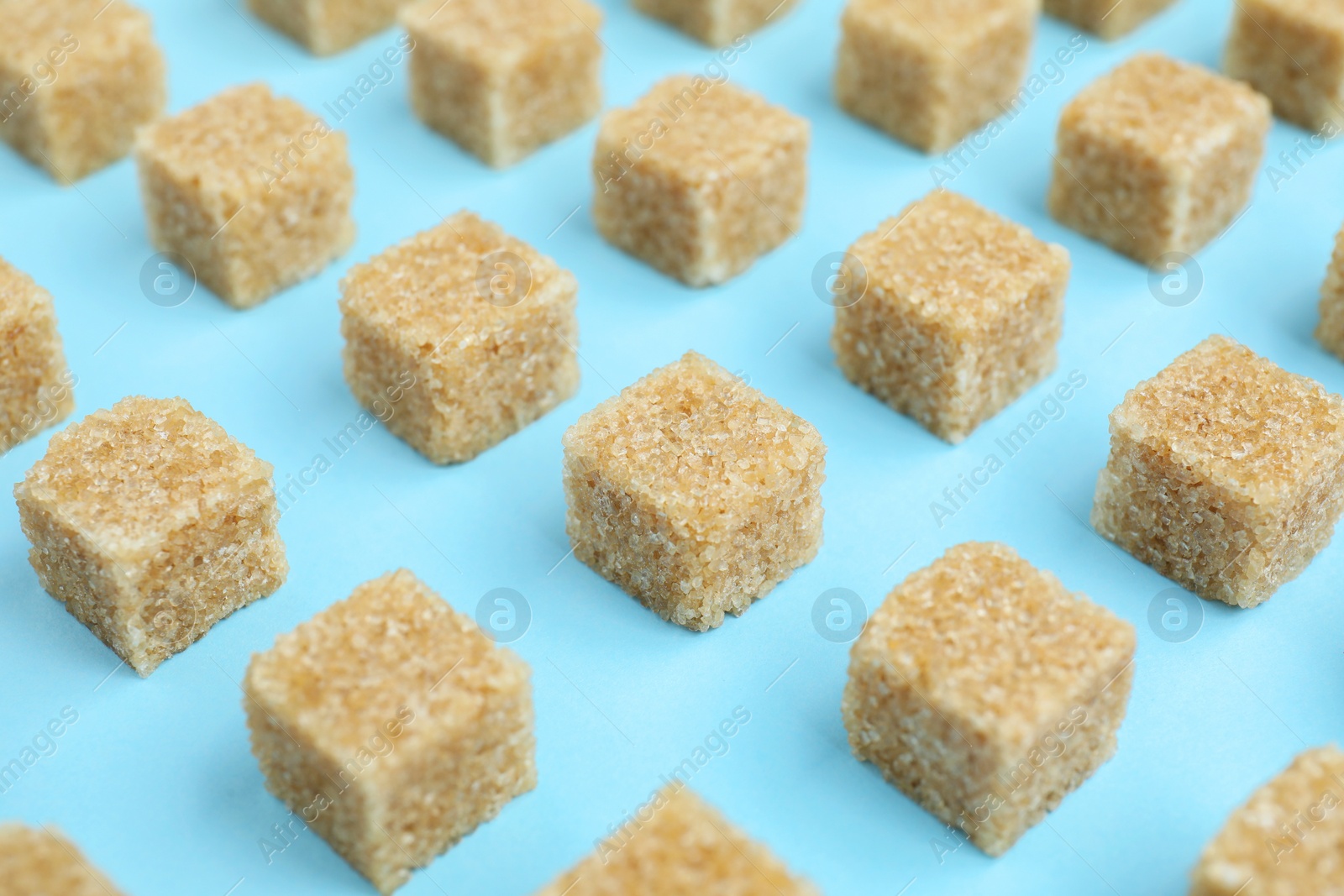 Photo of Brown sugar cubes on light blue background, closeup