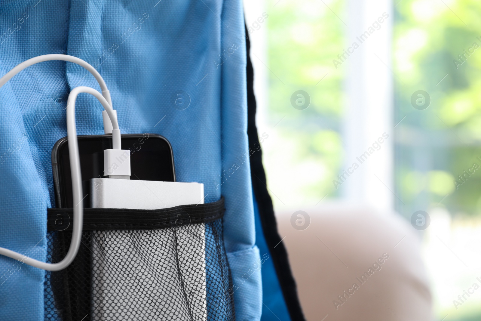 Photo of Charging mobile phone with power bank in light blue backpack, closeup. Space for text