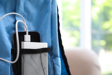 Photo of Charging mobile phone with power bank in light blue backpack, closeup. Space for text