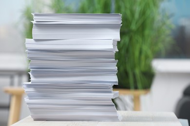 Stack of paper sheets on white wooden table against blurred background. Space for text