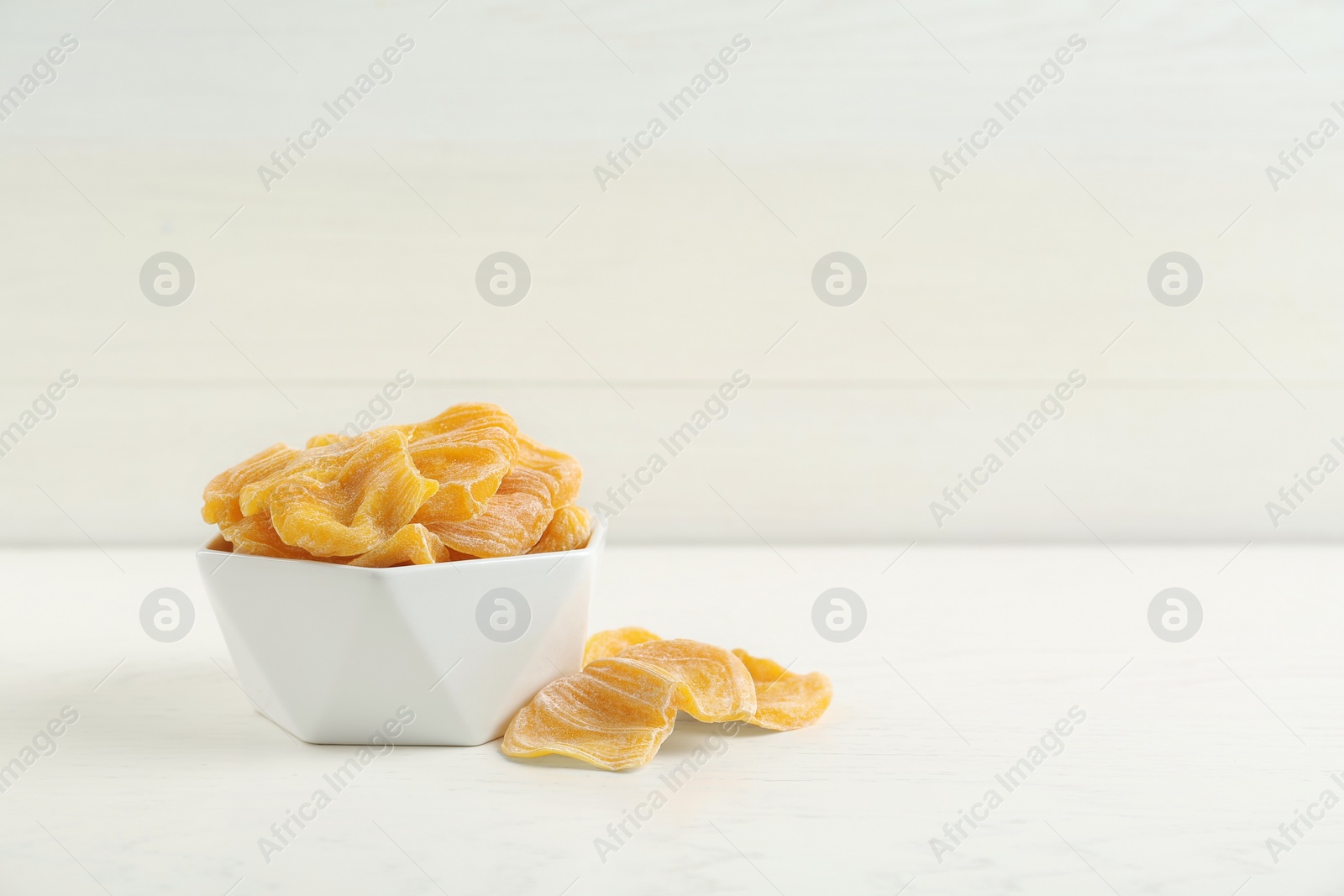 Photo of Delicious dried jackfruit slices in bowl on white wooden table. Space for text