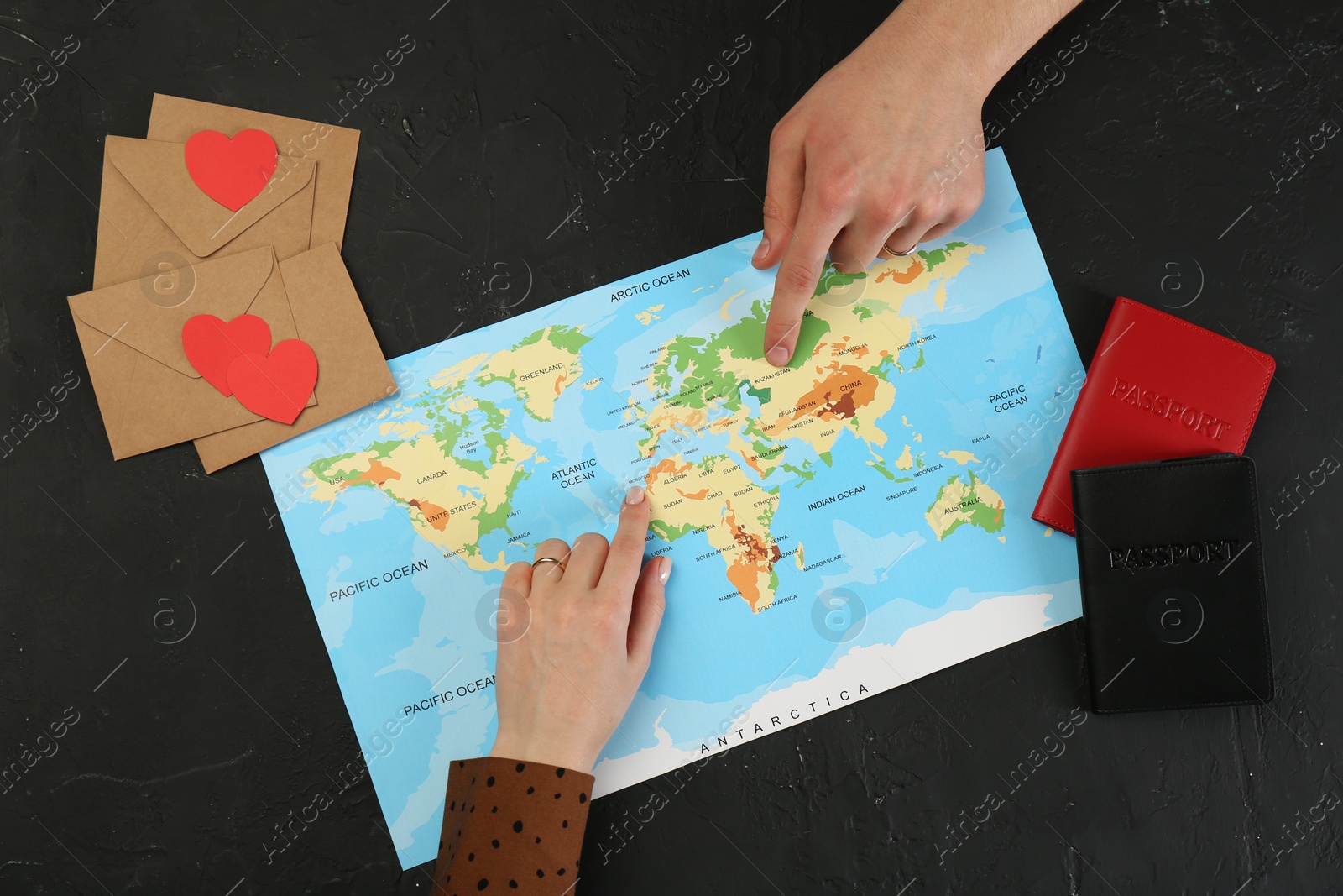 Photo of Man and woman planning their honeymoon trip with world map at black table, top view