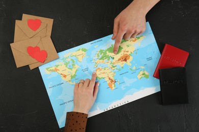 Man and woman planning their honeymoon trip with world map at black table, top view