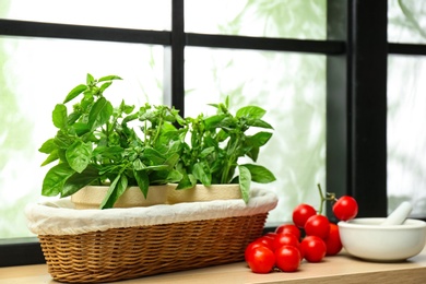 Green basil, tomatoes and mortar with pestle on window sill indoors