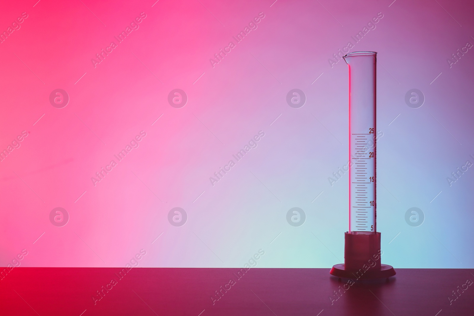 Photo of Empty graduated cylinder on table against color background. Chemistry laboratory glassware