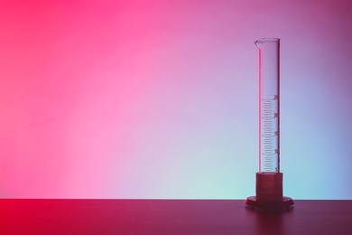 Photo of Empty graduated cylinder on table against color background. Chemistry laboratory glassware