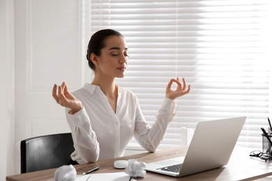 Photo of Young businesswoman meditating at workplace. Stress relief exercise