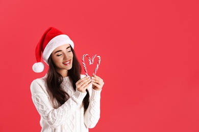 Photo of Beautiful woman in Santa Claus hat making heart with candy canes on red background. Space for text