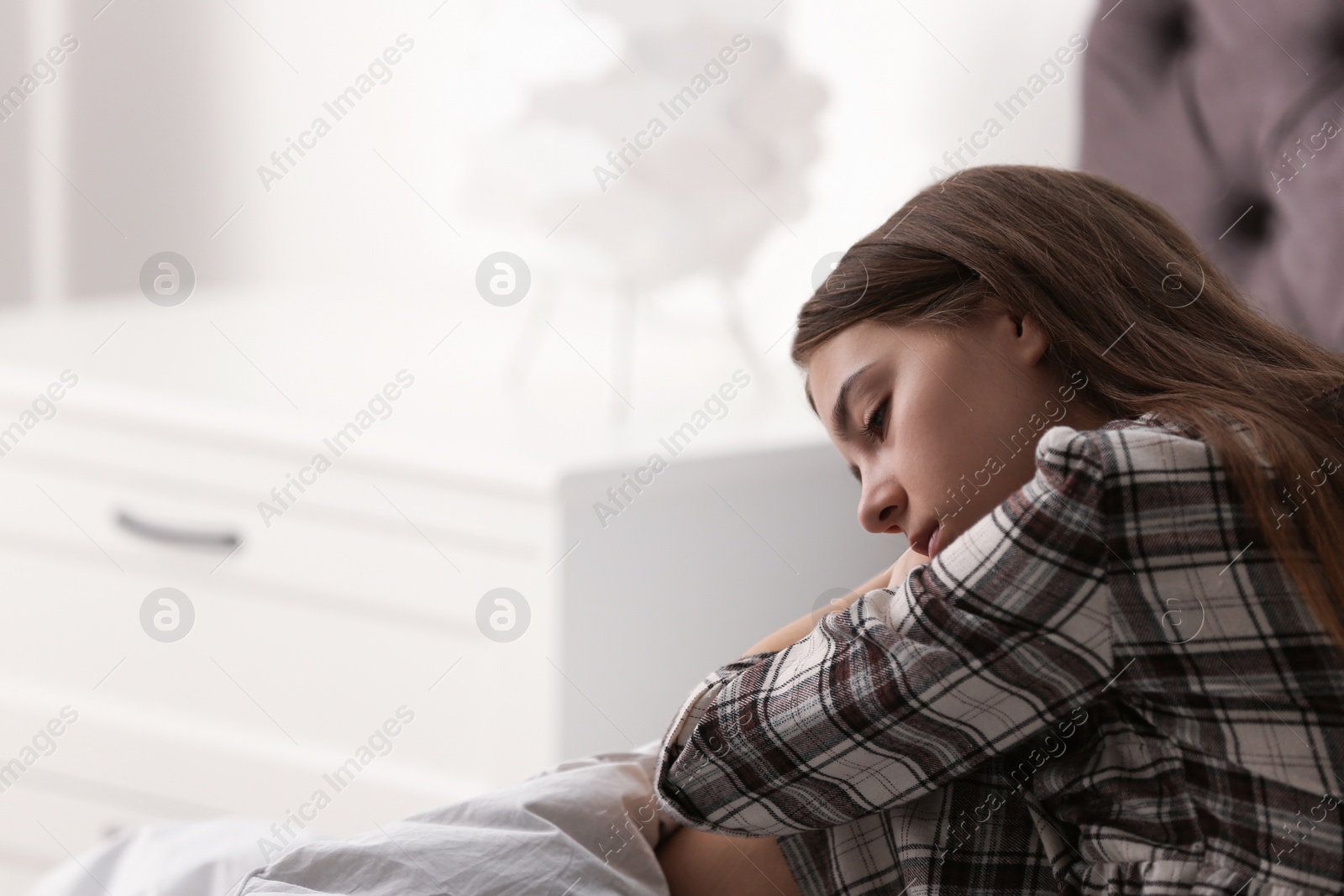 Photo of Upset teenage girl sitting on bed. Space for text