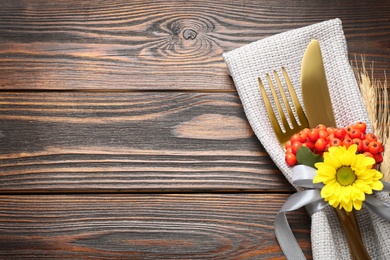 Photo of Cutlery, flower with rowan berries and space for text on wooden table, closeup. Thanksgiving Day celebration