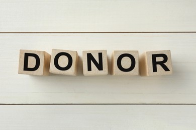 Photo of Word Donor made of cubes on white wooden table, top view