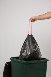 Photo of Man throwing garbage bag into bin on light background, closeup
