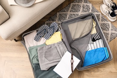 Photo of Open suitcase with different men clothes and accessories on floor, top view