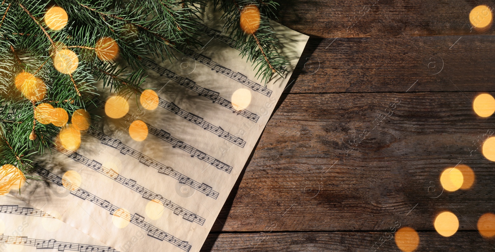 Image of Christmas greeting card design. Music sheets and fir tree on wooden background, top view with space for text