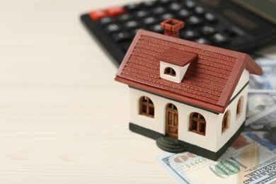Photo of Mortgage concept. House model, calculator and money on white wooden table, closeup with space for text