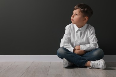 Photo of Little boy sitting on floor near black wall, space for text. School bullying