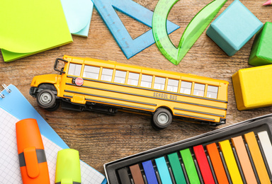 Photo of Flat lay composition with yellow school bus model on wooden background. Transport for students