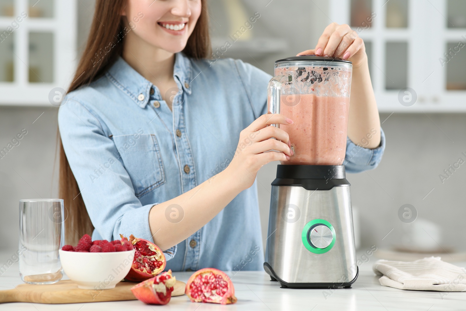 Photo of Beautiful young woman preparing tasty smoothie at white table in kitchen, closeup