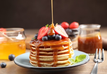 Photo of Pouring caramel syrup onto fresh pancakes with berries on wooden table