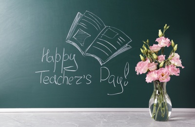 Green chalkboard with inscription HAPPY TEACHER'S DAY and vase of flowers on grey stone table