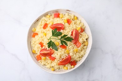 Tasty couscous with parsley, corn and tomatoes in bowl on white marble table, top view