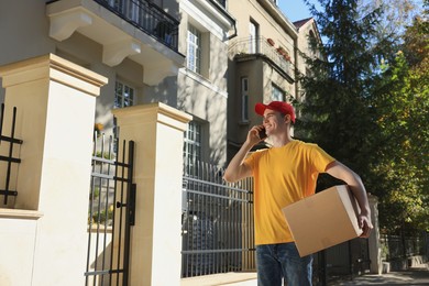 Photo of Courier with parcel talking by smartphone on city street