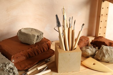 Photo of Clay and set of modeling tools on wooden table in workshop