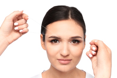 Young woman having eyebrow correction with thread on white background