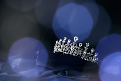 Beautiful silver tiara with diamonds on dark cloth against blurred lights, space for text