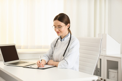 Photo of Young female doctor working at table in office