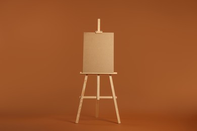 Wooden easel with blank board on brown background