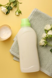 Photo of Bottle of fabric softener, towel, detergent powder and roses on pale yellow background, flat lay