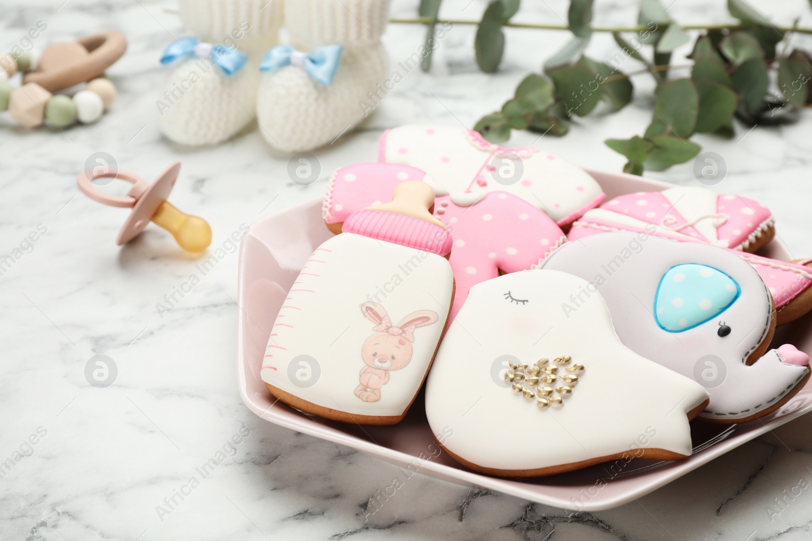 Photo of Plate of baby shower cookies and accessories on white marble table, closeup