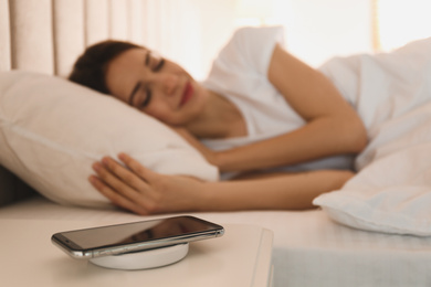 Photo of Smartphone charging on wireless pad and woman sleeping in bed