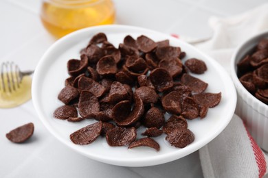 Photo of Breakfast cereal. Chocolate corn flakes and milk in bowl on white table, closeup