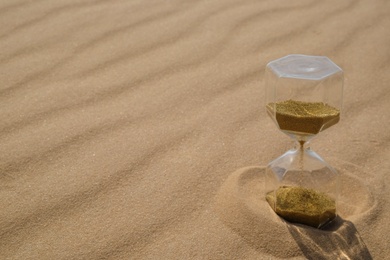 Photo of Hourglass with flowing sand in desert on sunny day. Space for text