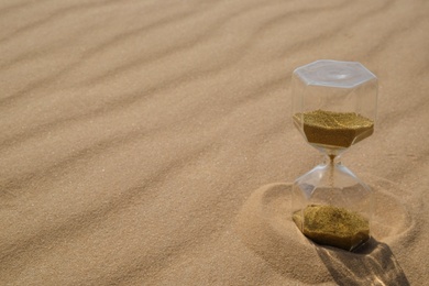 Hourglass with flowing sand in desert on sunny day. Space for text