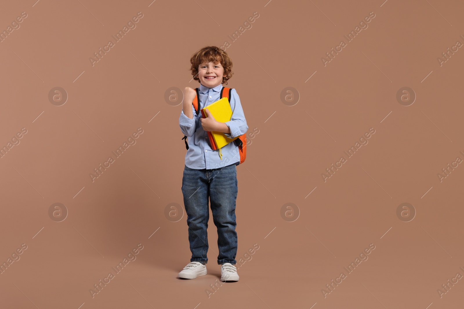 Photo of Happy schoolboy with backpack and books on brown background