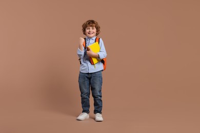 Happy schoolboy with backpack and books on brown background