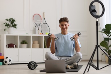 Smiling sports blogger working out with dumbbells while streaming online fitness lesson at home