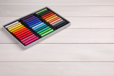 Photo of Set of colorful pastels in box on white wooden table, space for text. Drawing materials