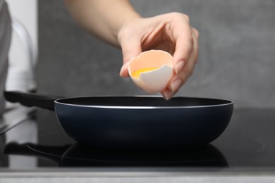 Photo of Woman breaking egg into frying pan, closeup