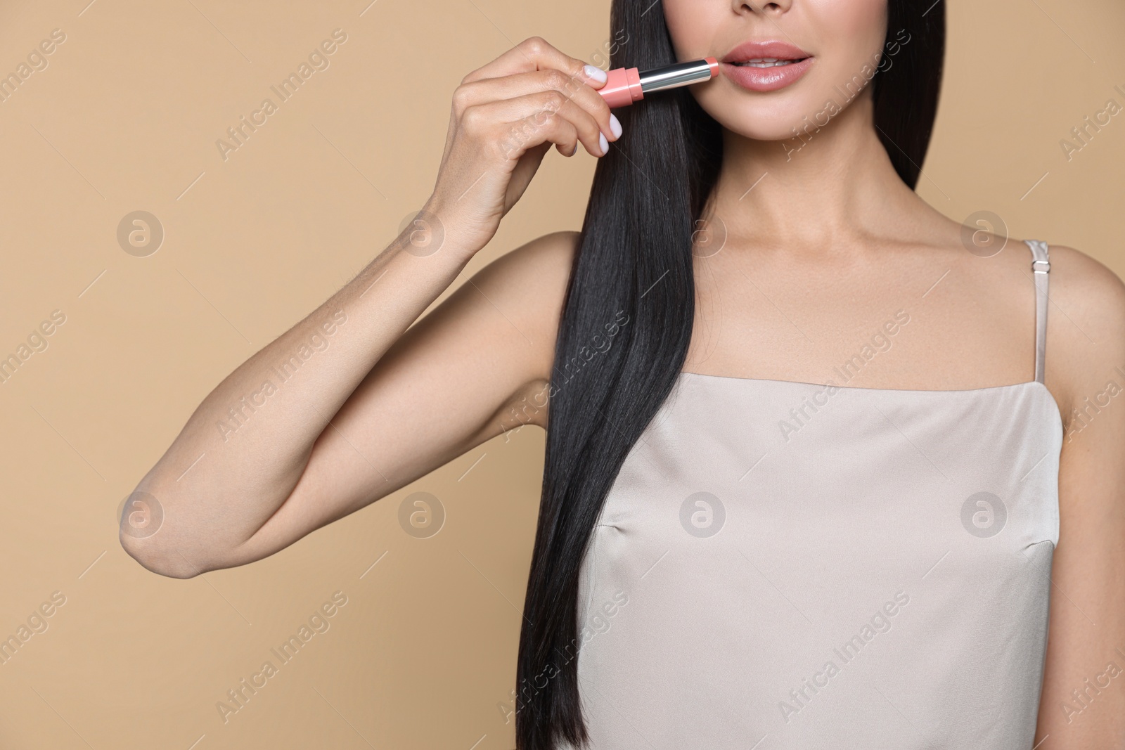 Photo of Young woman with beautiful makeup holding nude lipstick on beige background, closeup