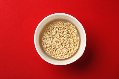 Photo of Cup of instant noodles on color background, top view